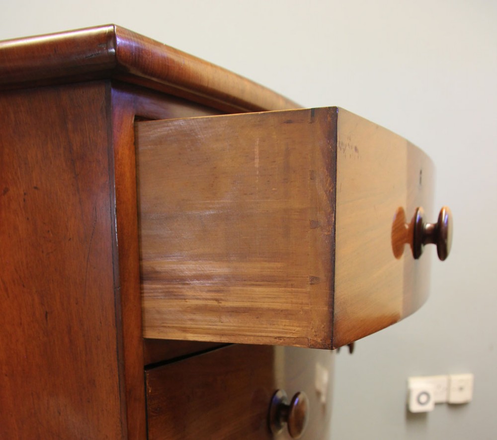 A Victorian mahogany bow front chest of drawers featuring a two over three drawer layout with turned wooden handles and a curved plinth base. View VIII