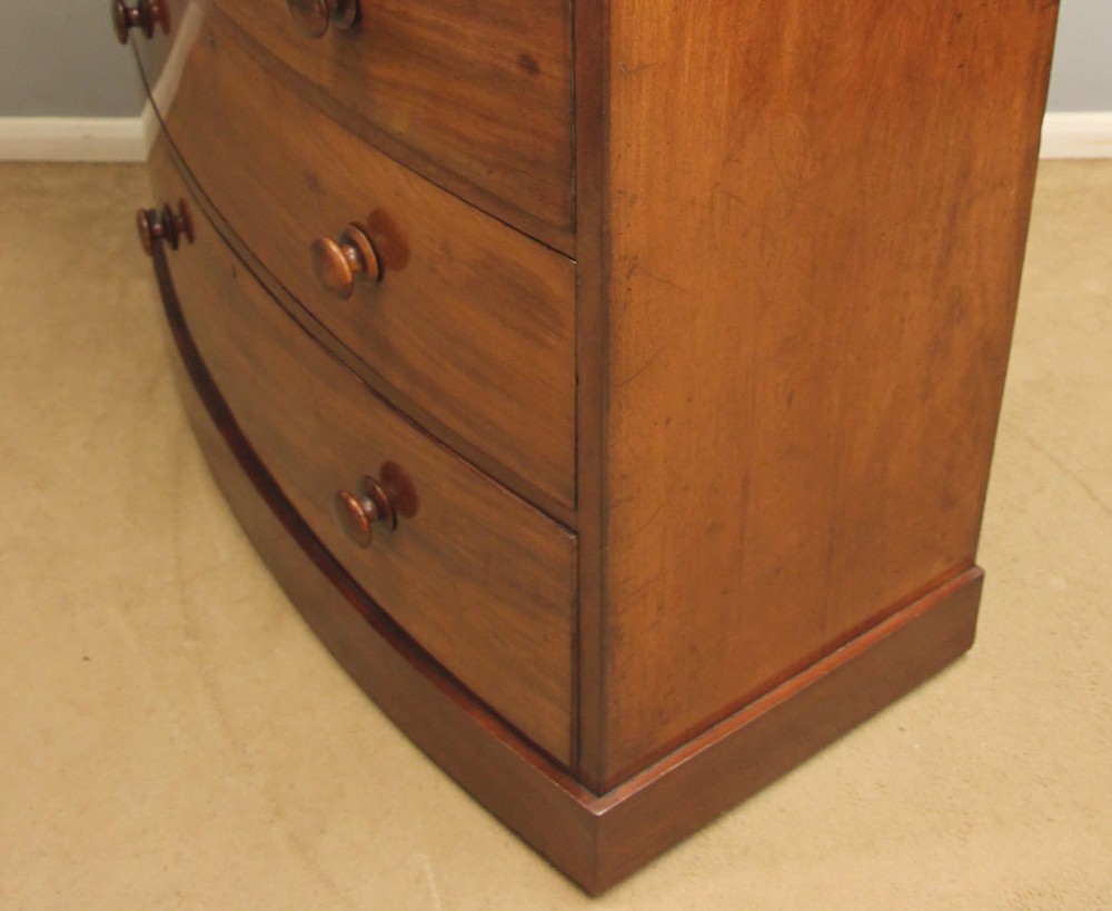 A Victorian mahogany bow front chest of drawers featuring a two over three drawer layout with turned wooden handles and a curved plinth base. View X