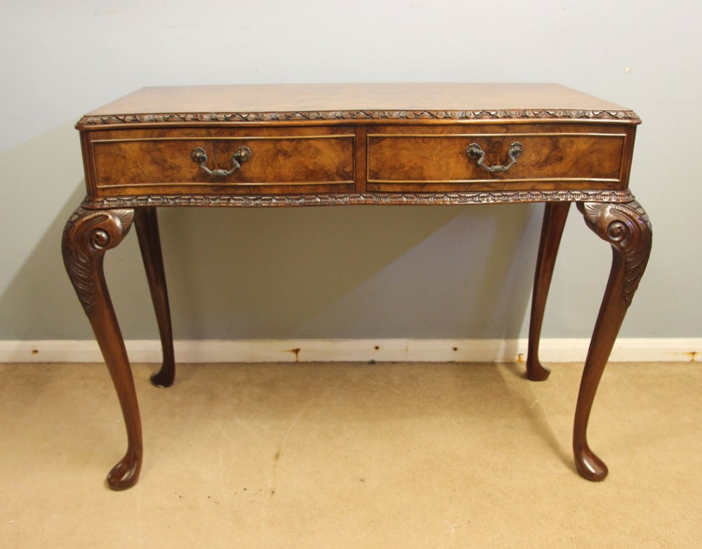 An antique walnut side table featuring two veneered drawer fronts, carved edge moulding, brass handles, and slender cabriole legs with carved knees.