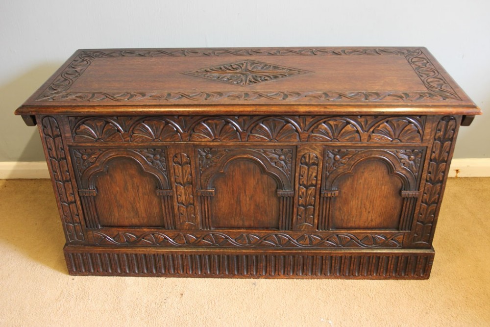 A carved dark oak coffer featuring three carved arch panels on the front facade and a central diamond motif on the hinged lid.