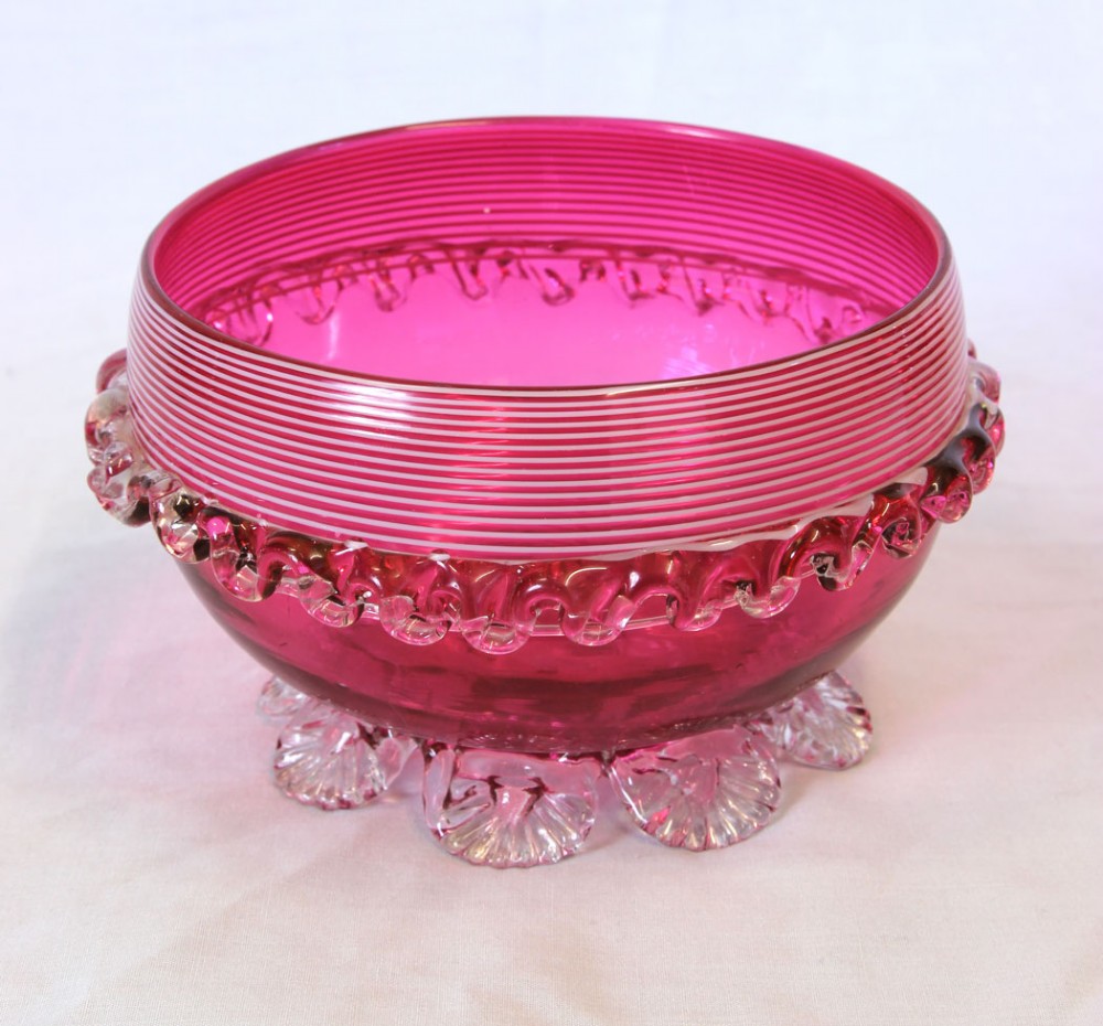 A Victorian cranberry pink glass bowl featuring fine horizontal white threading, an applied clear frilled band, and shell-shaped clear glass feet.