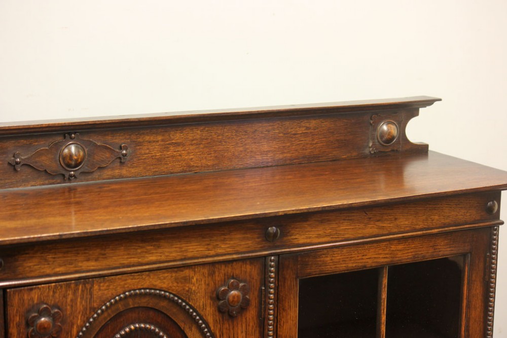 An antique dark oak low bookcase featuring twin glazed outer doors, a central carved oval timber door, and heavy bun feet. View IV
