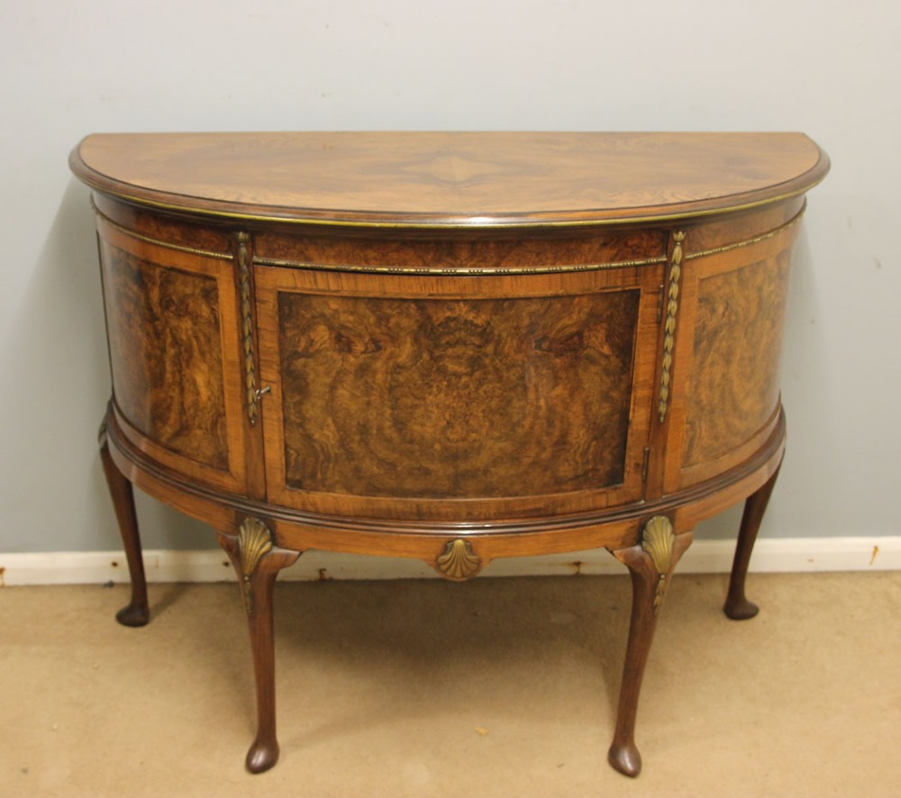 A semi-circular burr walnut side cabinet featuring cabriole legs with shell carvings and brass mounts.