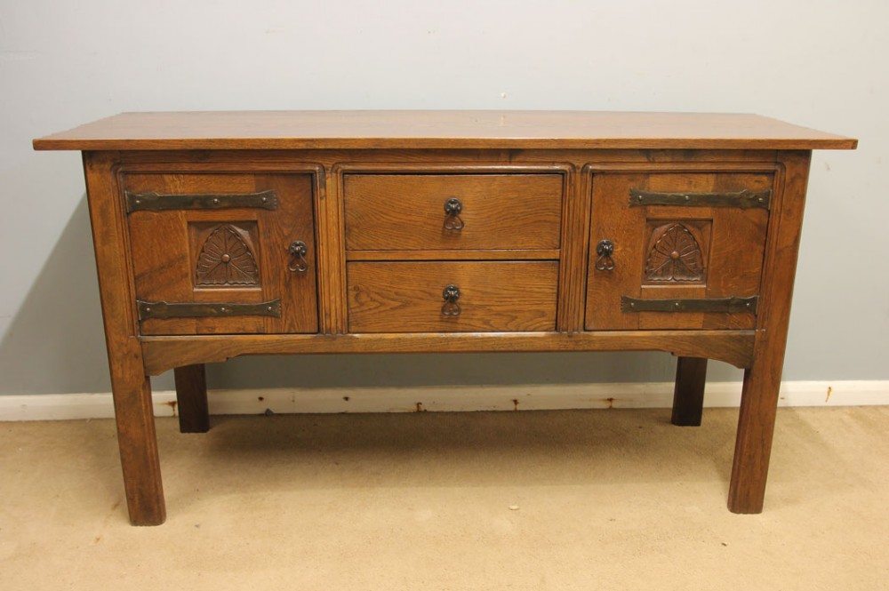 An antique oak sideboard with two central drawers, two carved panel doors with iron strap hinges, and sturdy square legs.