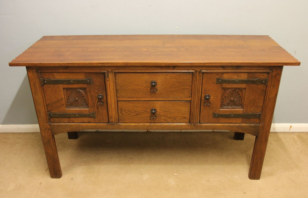 An antique oak sideboard with two central drawers, two carved panel doors with iron strap hinges, and sturdy square legs. View II