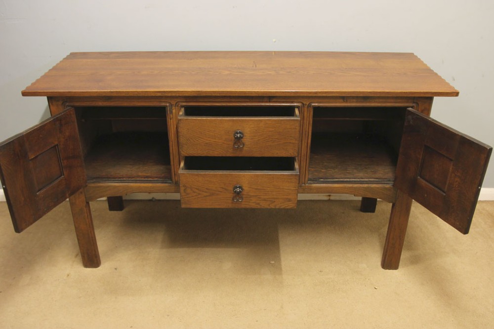 An antique oak sideboard with two central drawers, two carved panel doors with iron strap hinges, and sturdy square legs. View VII