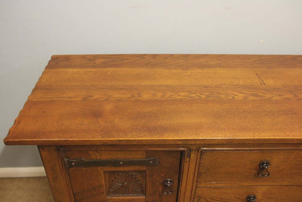 An antique oak sideboard with two central drawers, two carved panel doors with iron strap hinges, and sturdy square legs. View IX