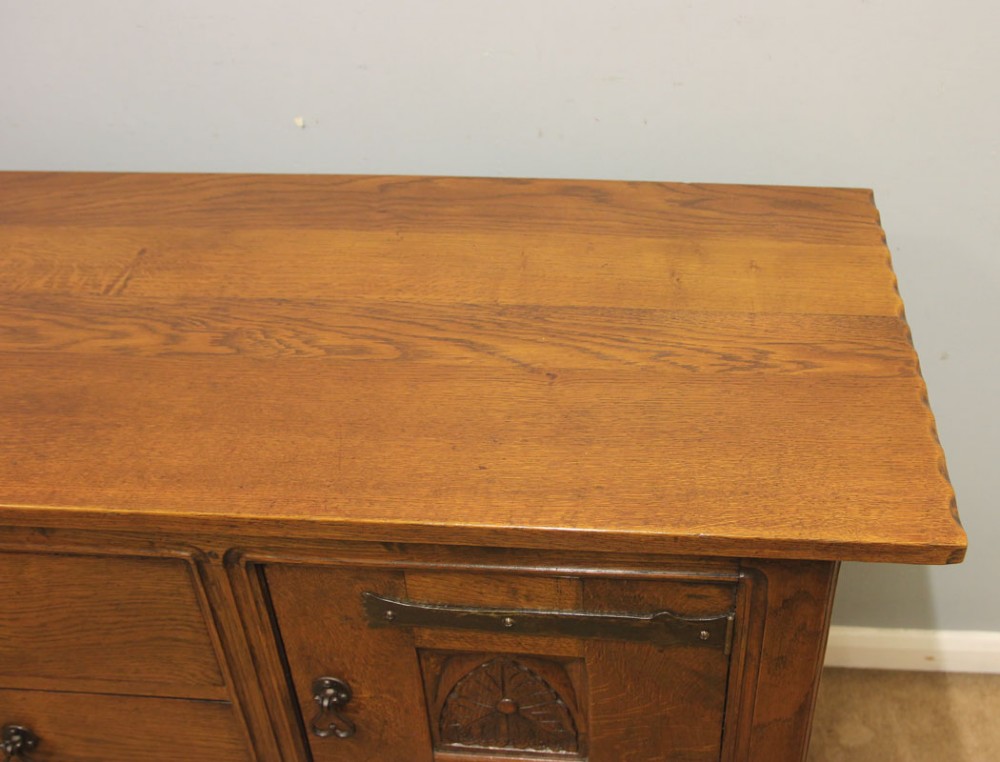 An antique oak sideboard with two central drawers, two carved panel doors with iron strap hinges, and sturdy square legs. View X