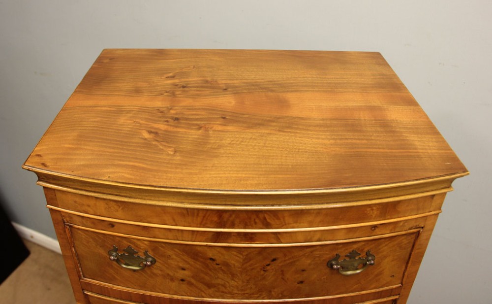 A tall bowfront burr walnut chest on chest featuring six drawers with brass drop handles and bracket feet. View III