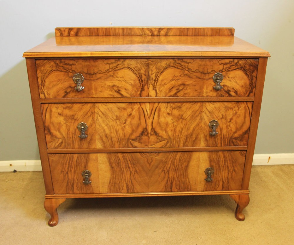 An antique figured walnut chest of drawers featuring three long drawers with decorative metal drop handles, supported on cabriole legs with a low gallery top.