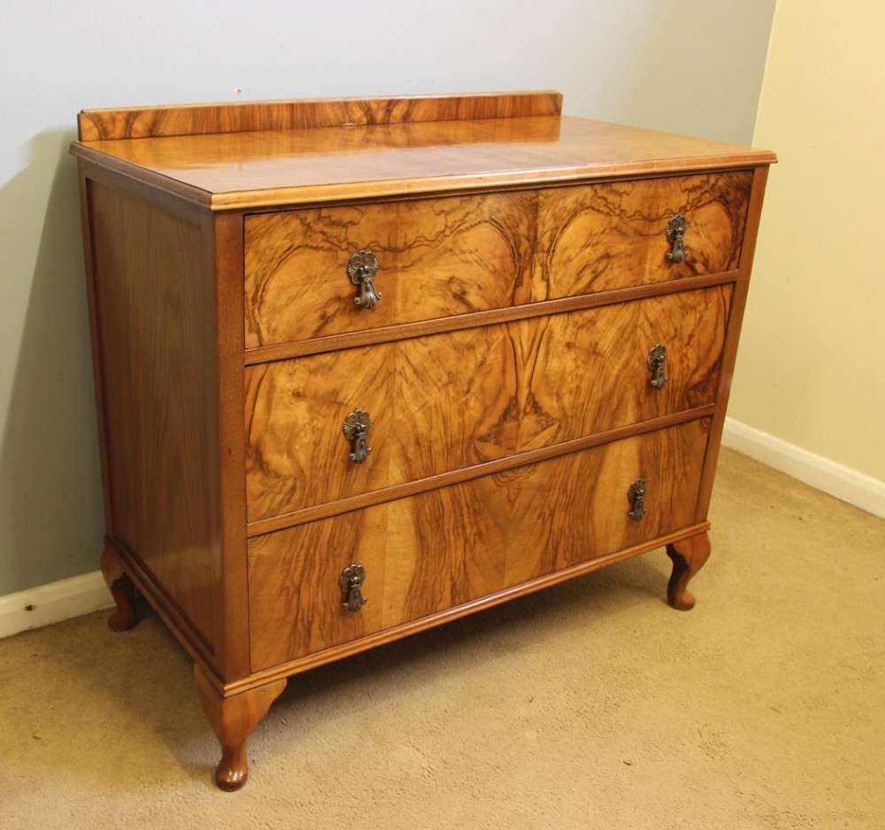 An antique figured walnut chest of drawers featuring three long drawers with decorative metal drop handles, supported on cabriole legs with a low gallery top. View II