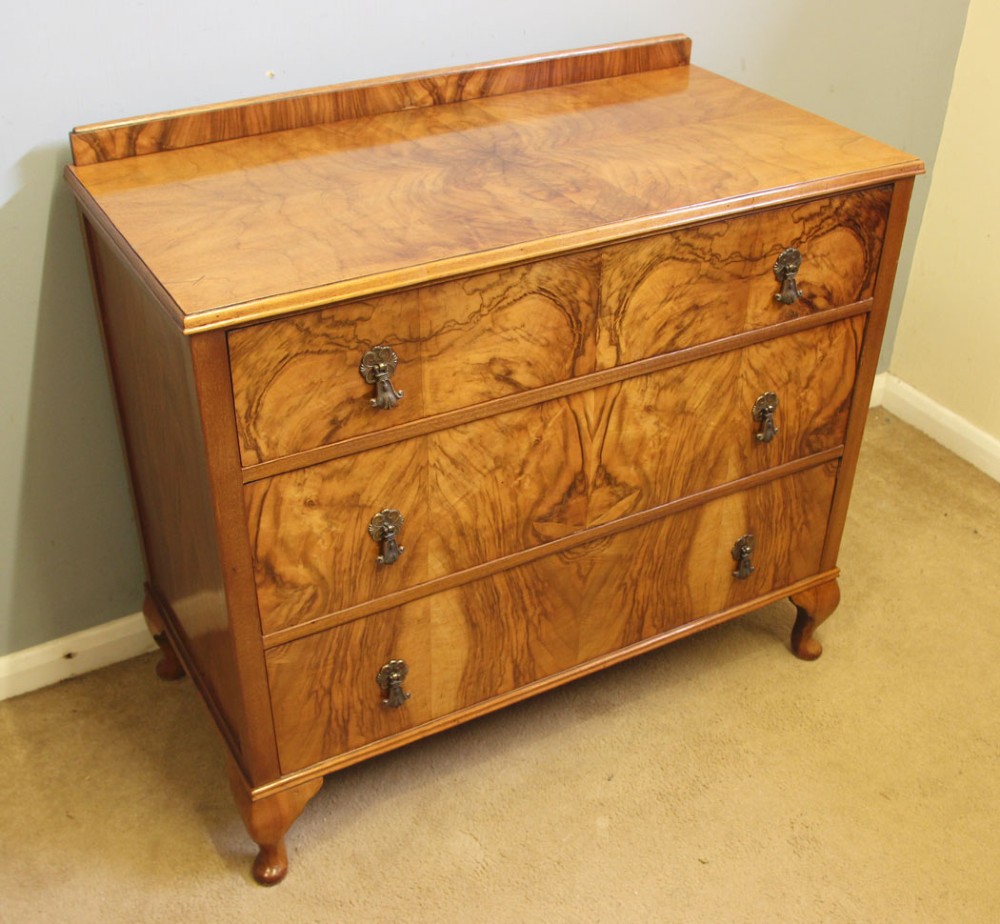 An antique figured walnut chest of drawers featuring three long drawers with decorative metal drop handles, supported on cabriole legs with a low gallery top. View III