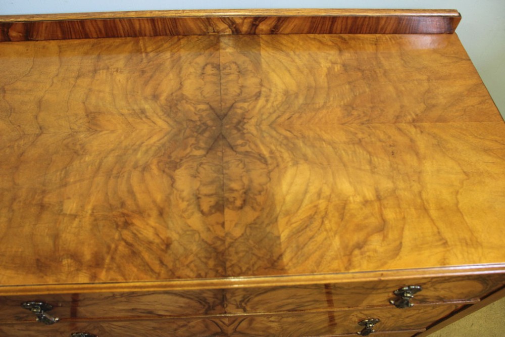 An antique figured walnut chest of drawers featuring three long drawers with decorative metal drop handles, supported on cabriole legs with a low gallery top. View IV