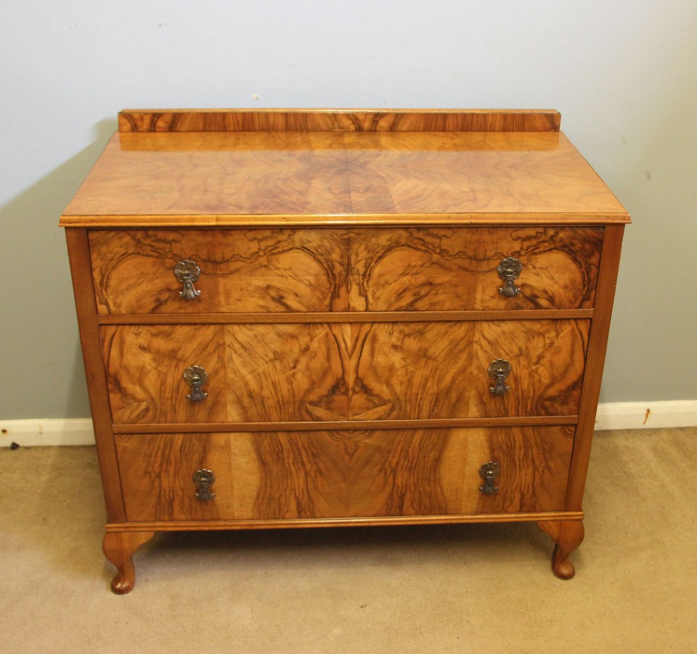 An antique figured walnut chest of drawers featuring three long drawers with decorative metal drop handles, supported on cabriole legs with a low gallery top. View VII