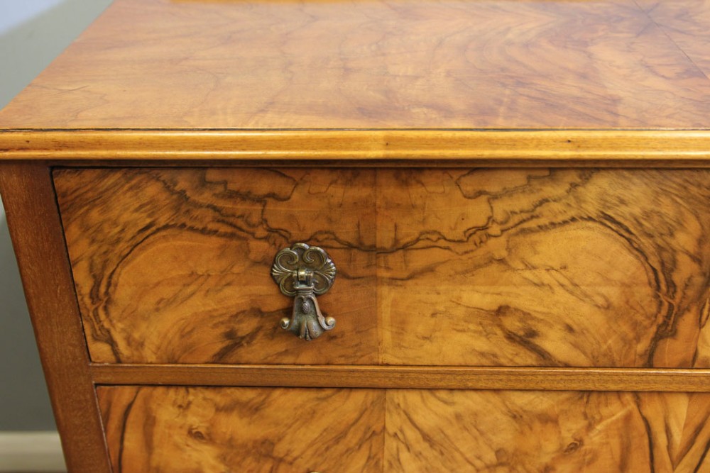 An antique figured walnut chest of drawers featuring three long drawers with decorative metal drop handles, supported on cabriole legs with a low gallery top. View IX
