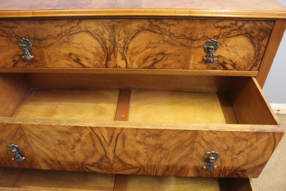 An antique figured walnut chest of drawers featuring three long drawers with decorative metal drop handles, supported on cabriole legs with a low gallery top. View X