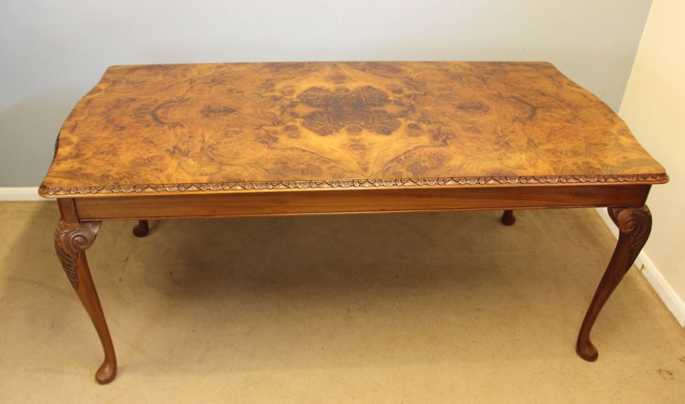 A rectangular burr walnut dining table featuring symmetrical book-matched veneer across the top, carved edge moulding, and cabriole legs.