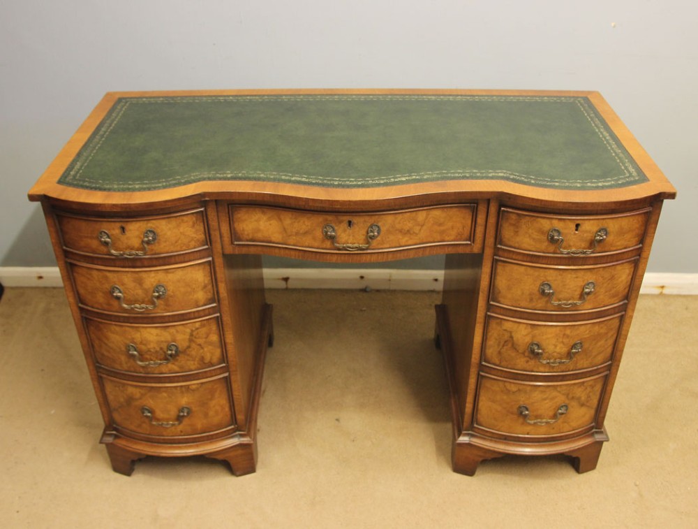 An antique burr walnut kneehole pedestal writing desk featuring a green leather inset top, nine drawers, and decorative brass handles. View II