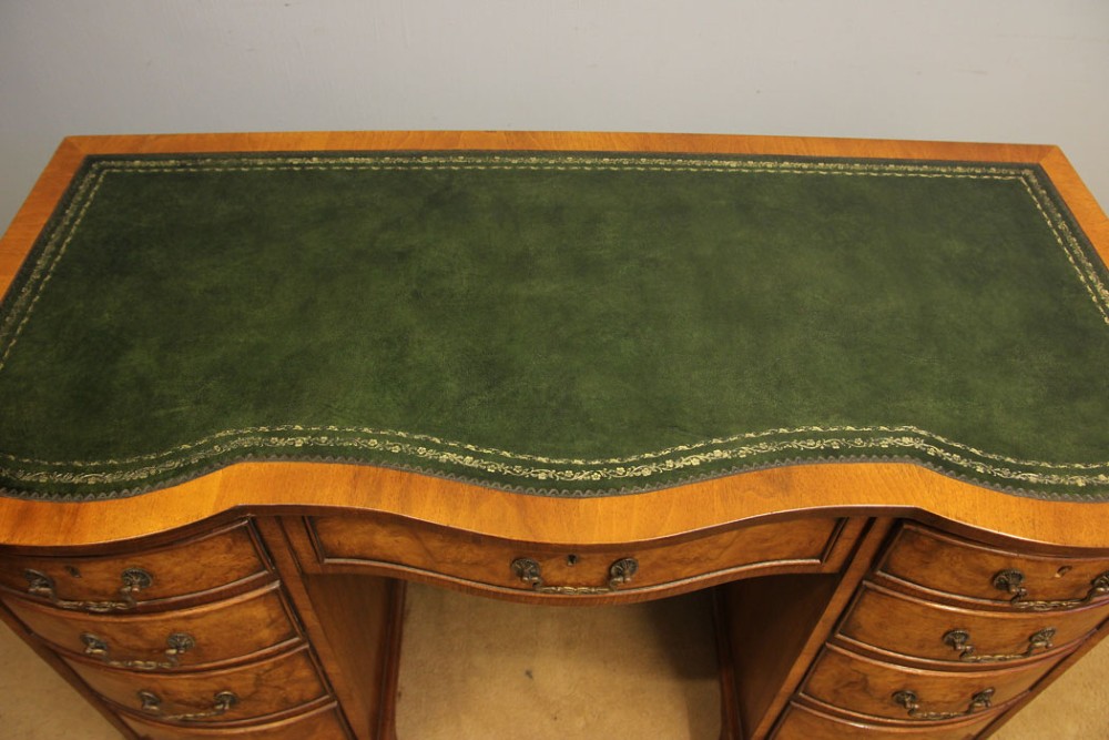 An antique burr walnut kneehole pedestal writing desk featuring a green leather inset top, nine drawers, and decorative brass handles. View III