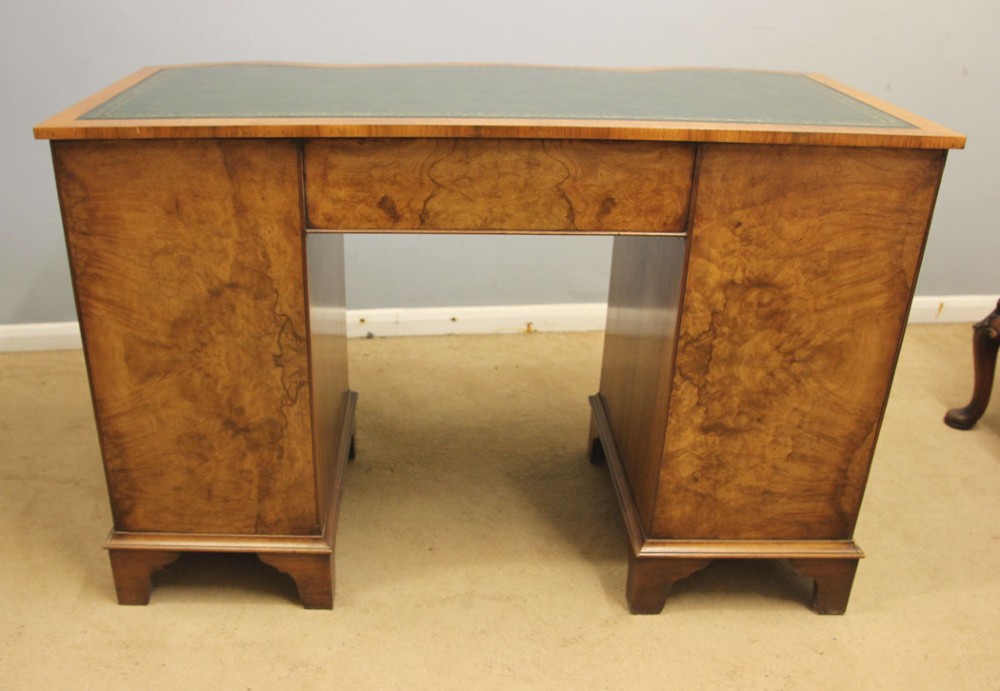 An antique burr walnut kneehole pedestal writing desk featuring a green leather inset top, nine drawers, and decorative brass handles. View VII