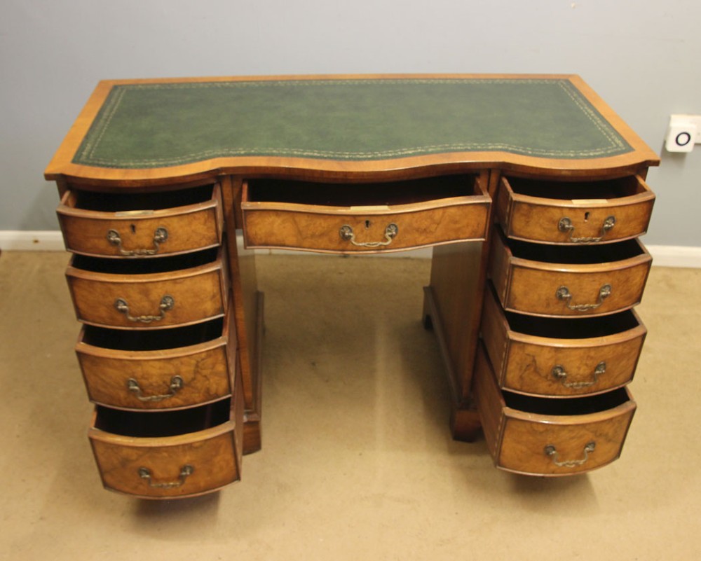 An antique burr walnut kneehole pedestal writing desk featuring a green leather inset top, nine drawers, and decorative brass handles. View VIII