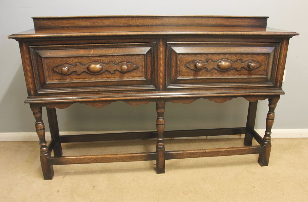 An antique dark oak side table with two geometric-panelled drawers, turned legs, a low stretcher base, and a raised backboard.