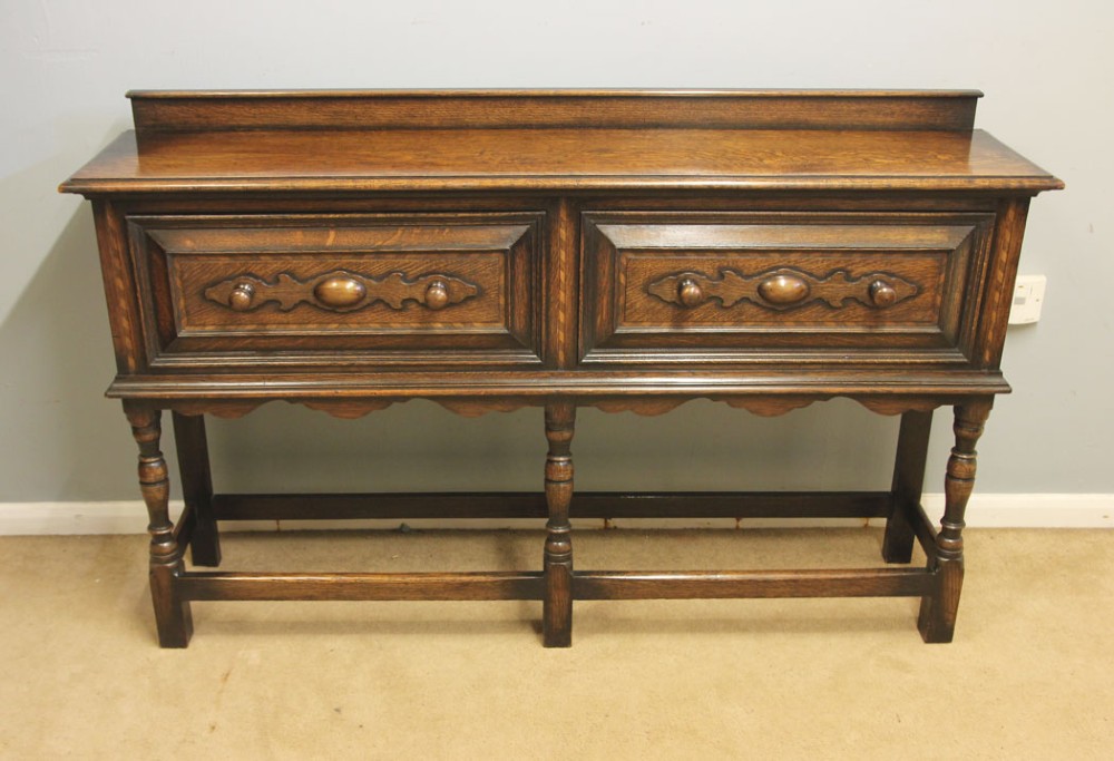 An antique dark oak side table with two geometric-panelled drawers, turned legs, a low stretcher base, and a raised backboard. View II