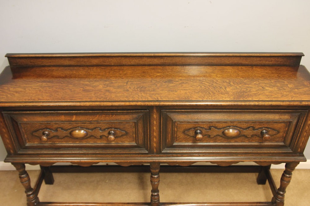 An antique dark oak side table with two geometric-panelled drawers, turned legs, a low stretcher base, and a raised backboard. View IV