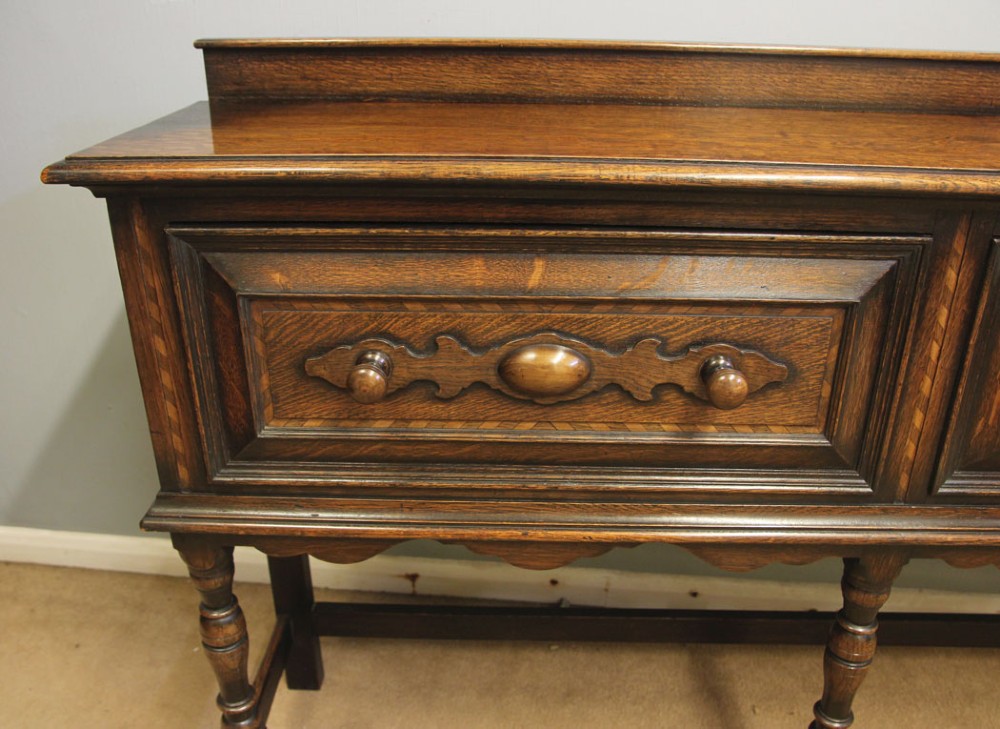 An antique dark oak side table with two geometric-panelled drawers, turned legs, a low stretcher base, and a raised backboard. View VI