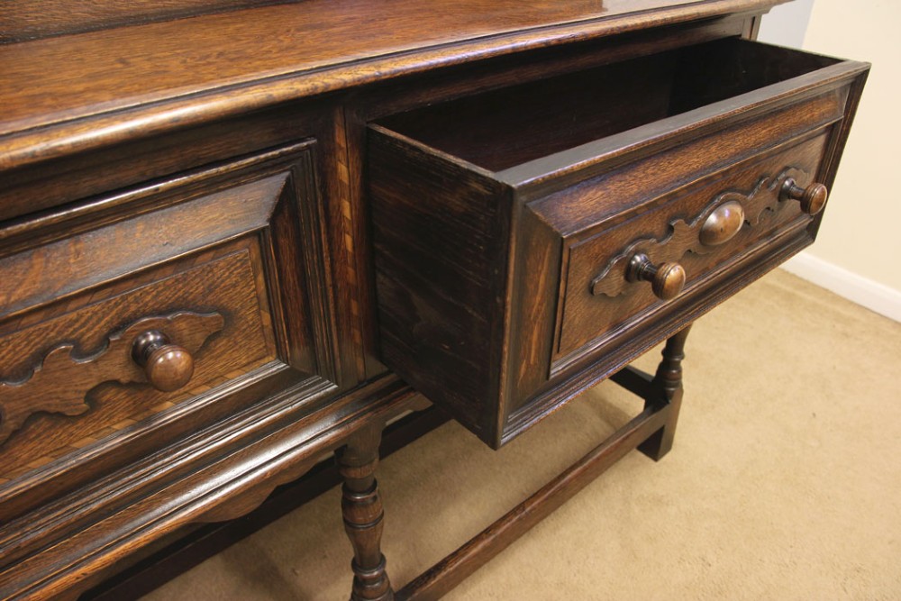 An antique dark oak side table with two geometric-panelled drawers, turned legs, a low stretcher base, and a raised backboard. View VII