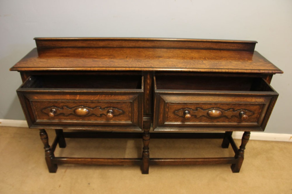 An antique dark oak side table with two geometric-panelled drawers, turned legs, a low stretcher base, and a raised backboard. View VIII