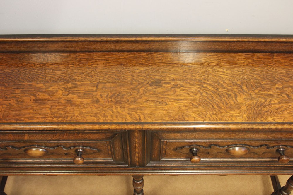An antique dark oak side table with two geometric-panelled drawers, turned legs, a low stretcher base, and a raised backboard. View X