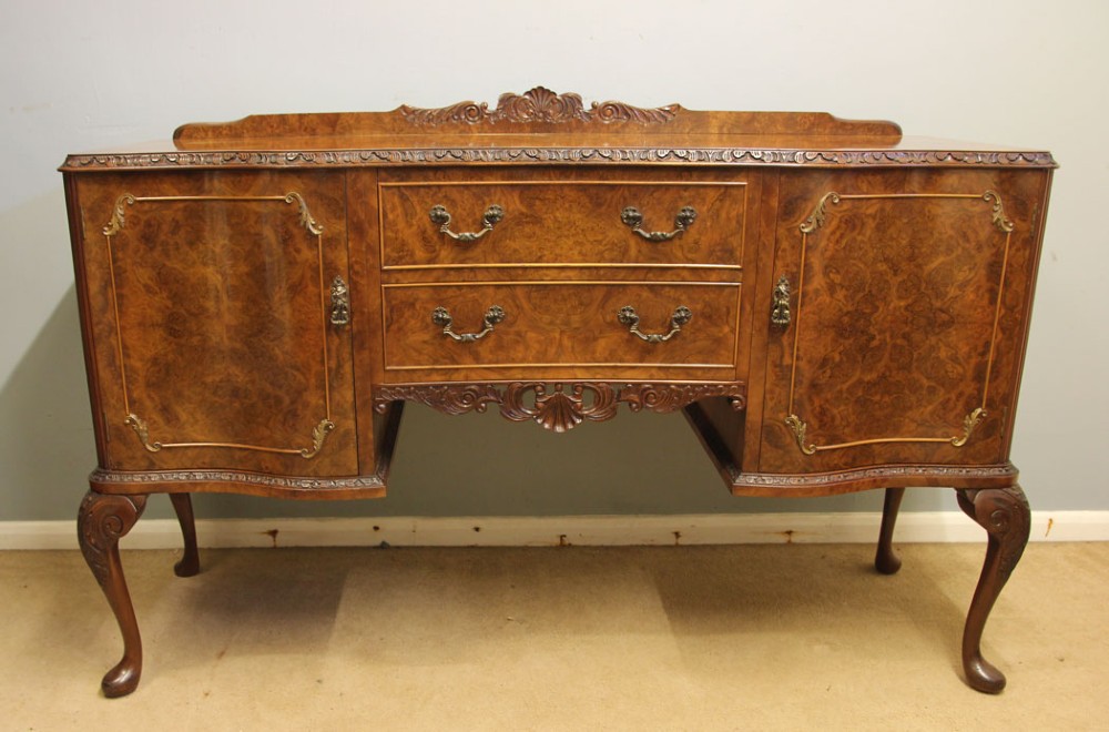 A burr walnut serpentine front sideboard featuring two central drawers flanked by side cupboards and raised on carved cabriole legs.