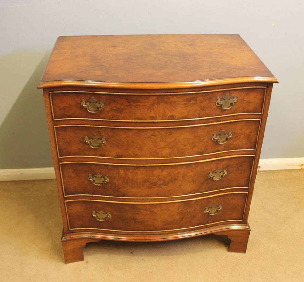 A burr walnut chest of drawers featuring four graduated drawers with a serpentine curved front, decorative brass handles, and resting on bracket feet. View II