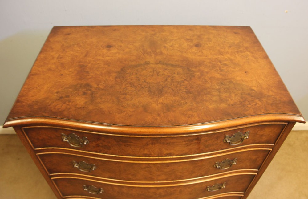 A burr walnut chest of drawers featuring four graduated drawers with a serpentine curved front, decorative brass handles, and resting on bracket feet. View IV