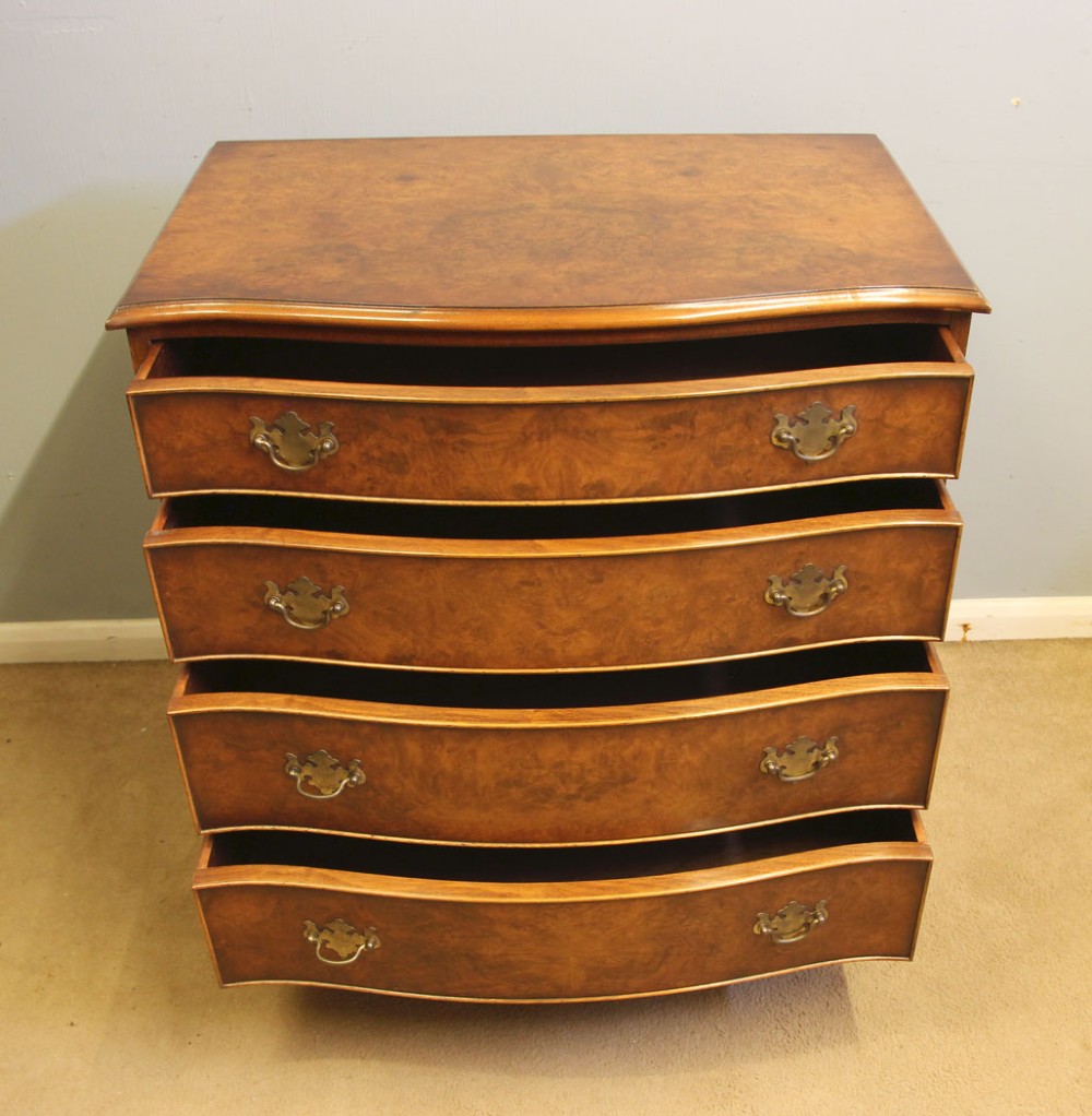 A burr walnut chest of drawers featuring four graduated drawers with a serpentine curved front, decorative brass handles, and resting on bracket feet. View V