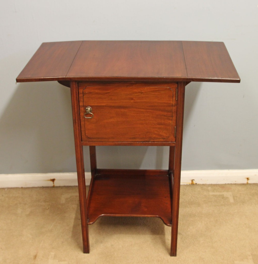 An antique mahogany bedside cabinet featuring two drop-leaf sides, a single door with a brass ring pull handle, straight legs, and an undertier shelf. View V