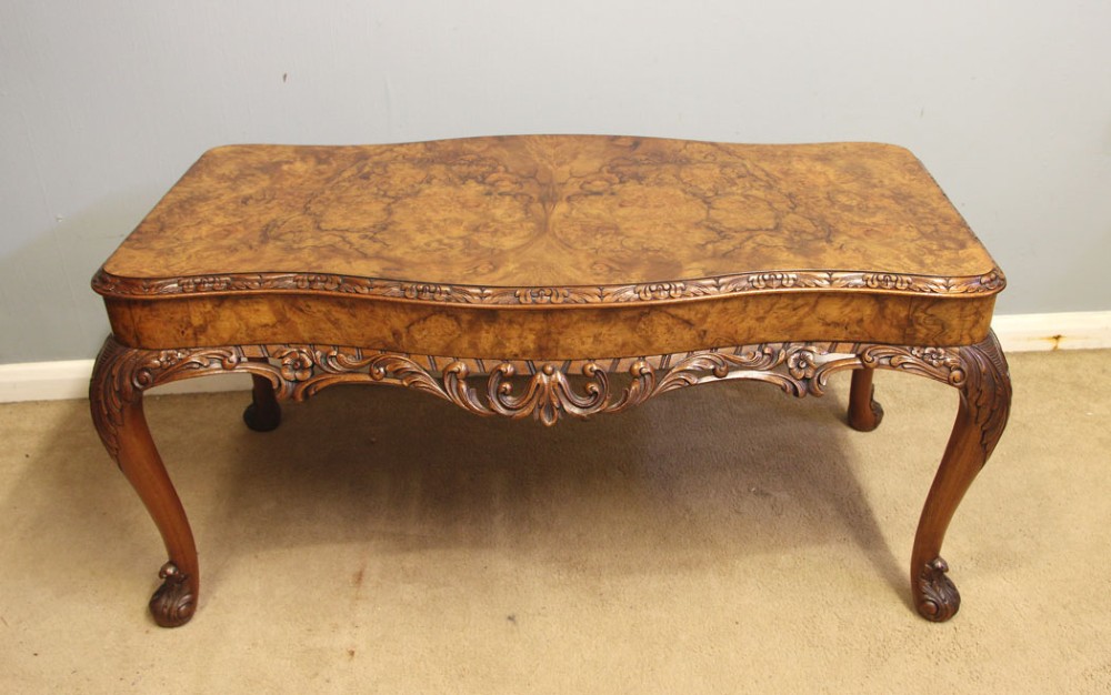 A low Queen Anne style burr walnut coffee table featuring carved cabriole legs, an ornate apron, and a serpentine book-matched top.