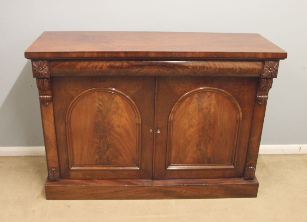 An antique Victorian flame mahogany chiffonier sideboard with two arched panel doors, carved corbels, and a plinth base. View II
