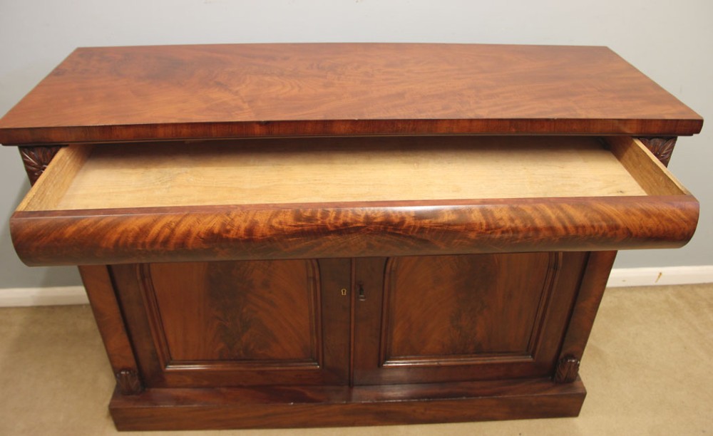 An antique Victorian flame mahogany chiffonier sideboard with two arched panel doors, carved corbels, and a plinth base. View IX