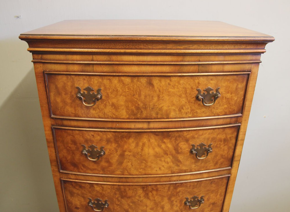 A tall burr walnut bow-front chest on chest featuring six stacked drawers, brass handles, and bracket feet. View III