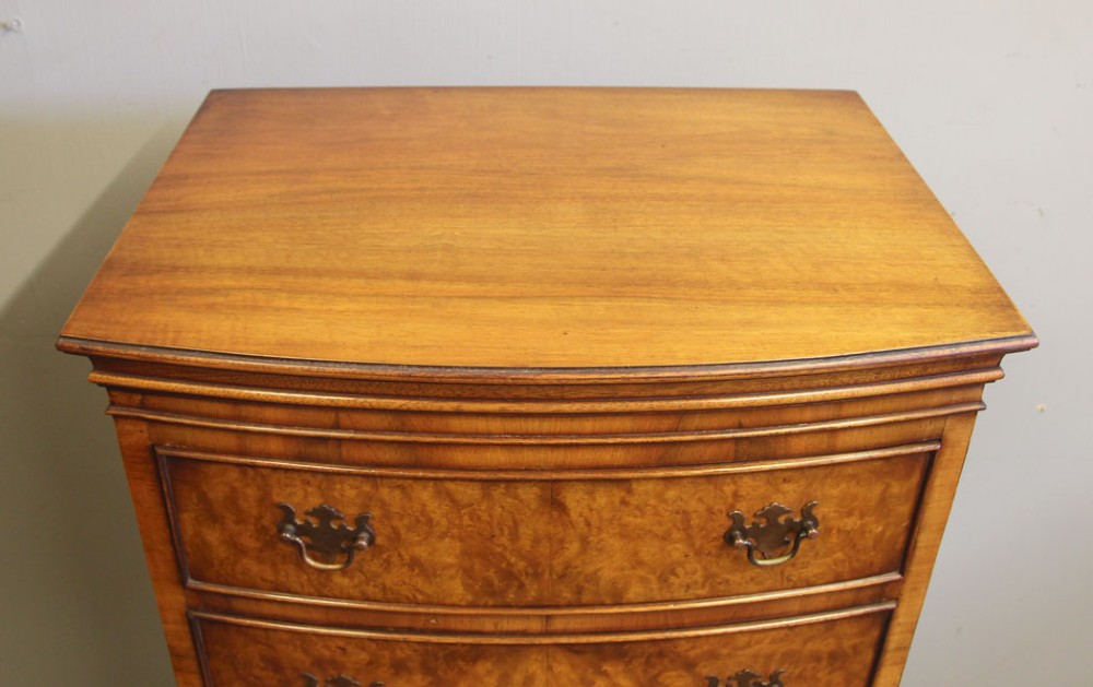 A tall burr walnut bow-front chest on chest featuring six stacked drawers, brass handles, and bracket feet. View VI