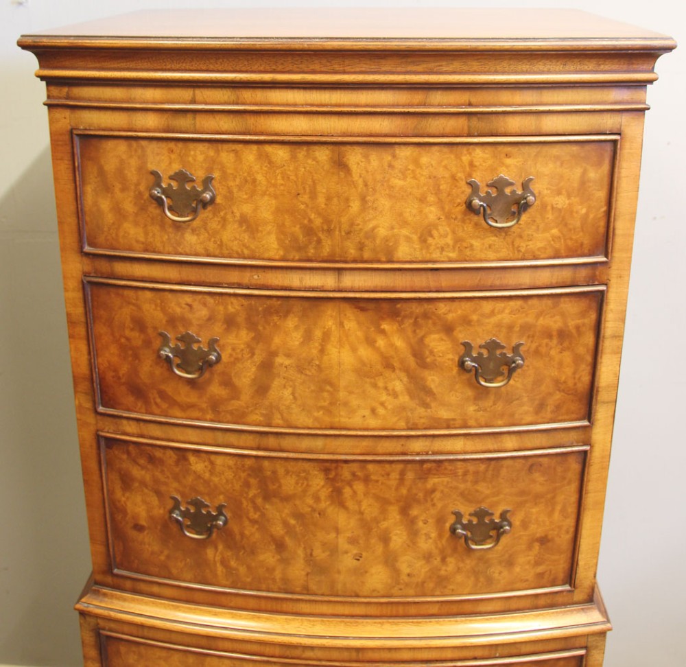 A tall burr walnut bow-front chest on chest featuring six stacked drawers, brass handles, and bracket feet. View IX