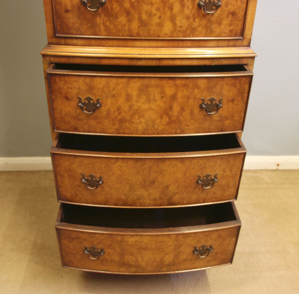 A tall burr walnut bow-front chest on chest featuring six stacked drawers, brass handles, and bracket feet. View XI