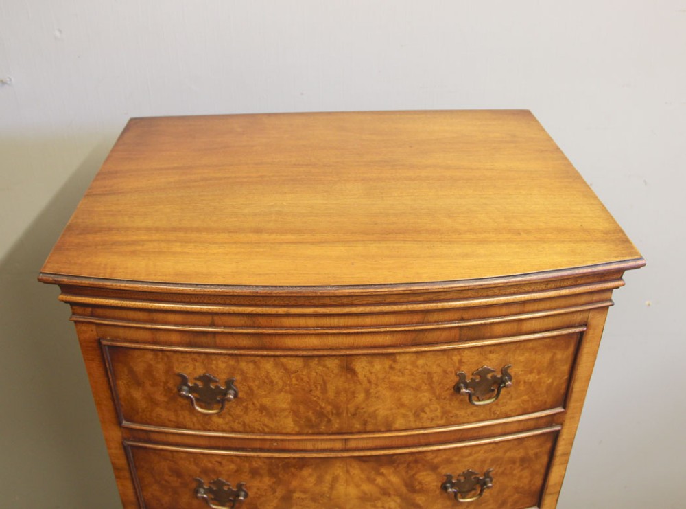 A tall burr walnut bow-front chest on chest featuring six stacked drawers, brass handles, and bracket feet. View XIII