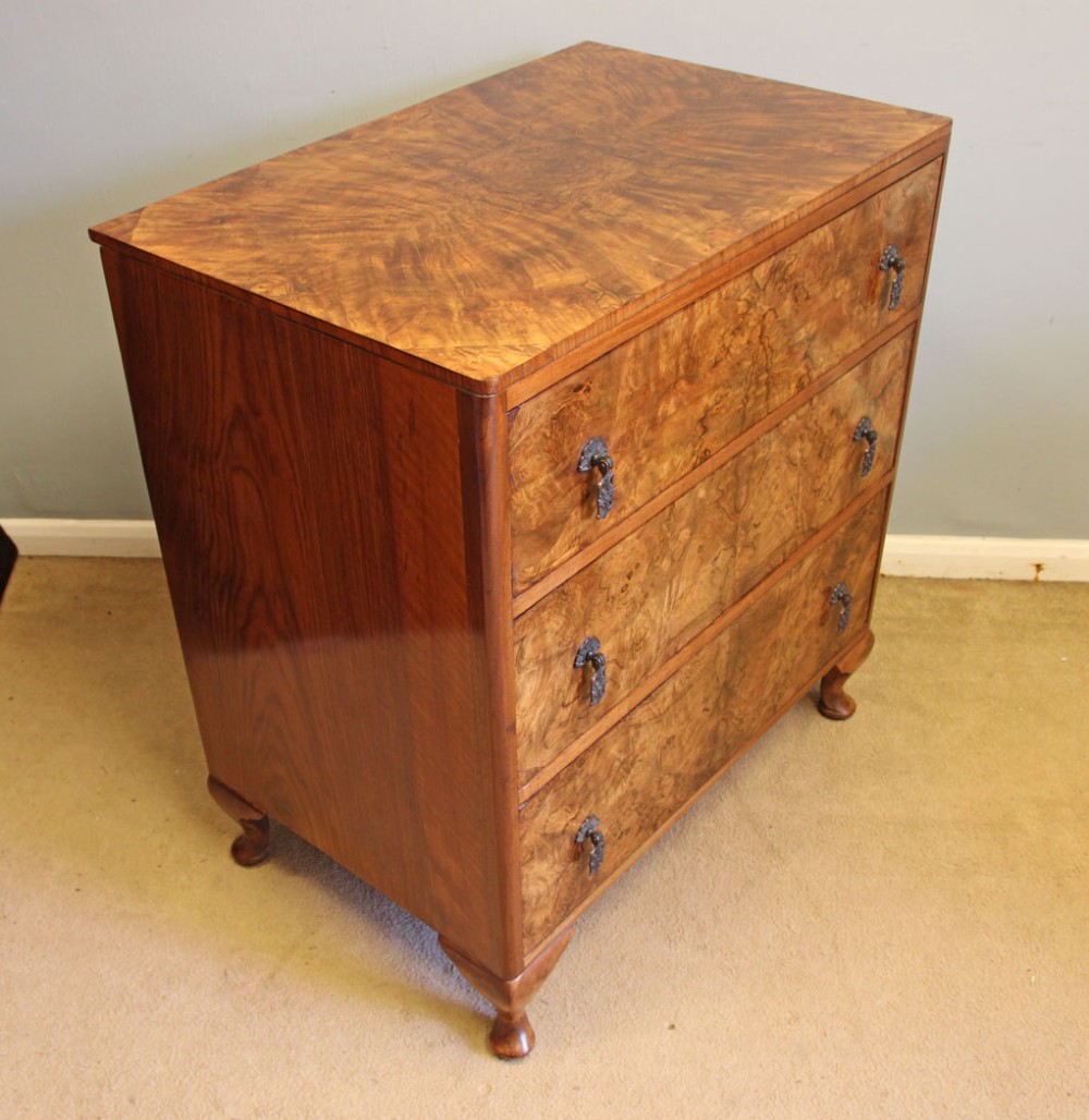 A three-drawer burr walnut chest of drawers featuring book-matched veneer patterns, ornate brass drop handles, and short cabriole legs. View III