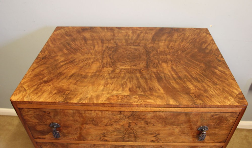 A three-drawer burr walnut chest of drawers featuring book-matched veneer patterns, ornate brass drop handles, and short cabriole legs. View VI
