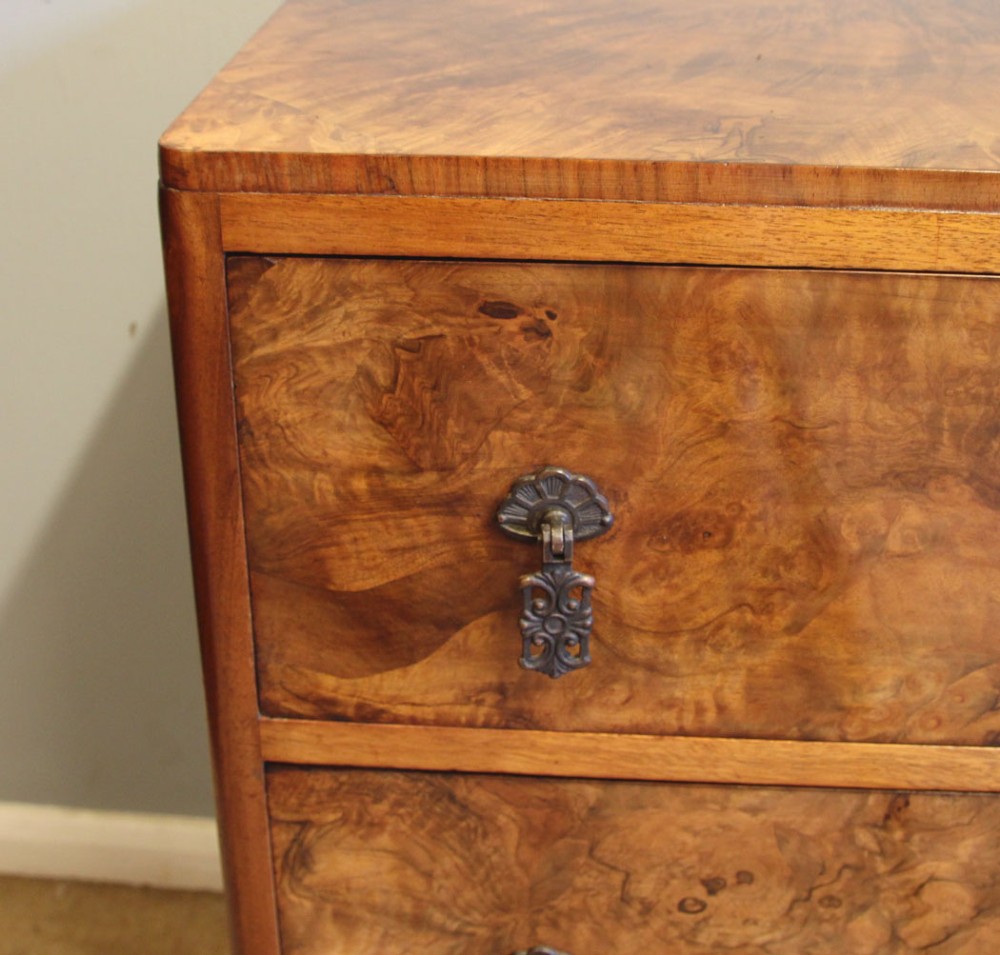A three-drawer burr walnut chest of drawers featuring book-matched veneer patterns, ornate brass drop handles, and short cabriole legs. View VII