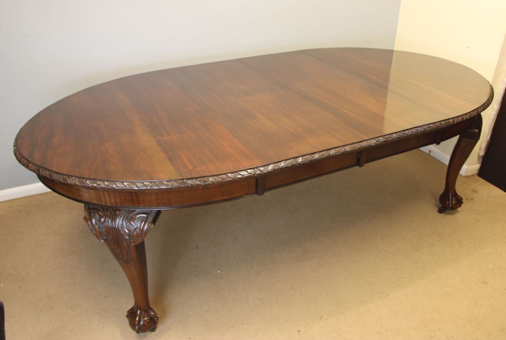 An oval mahogany extending dining table with two insert leaves, carved border edging, cabriole legs featuring acanthus knee carvings, and ball-and-claw feet.