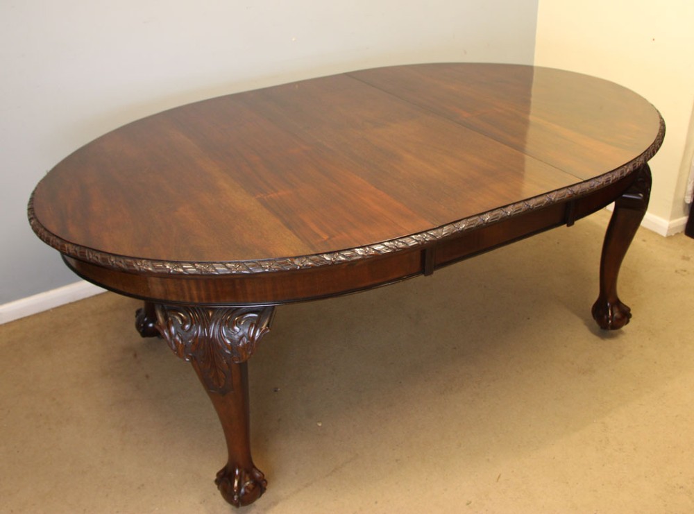 An oval mahogany extending dining table with two insert leaves, carved border edging, cabriole legs featuring acanthus knee carvings, and ball-and-claw feet. View III